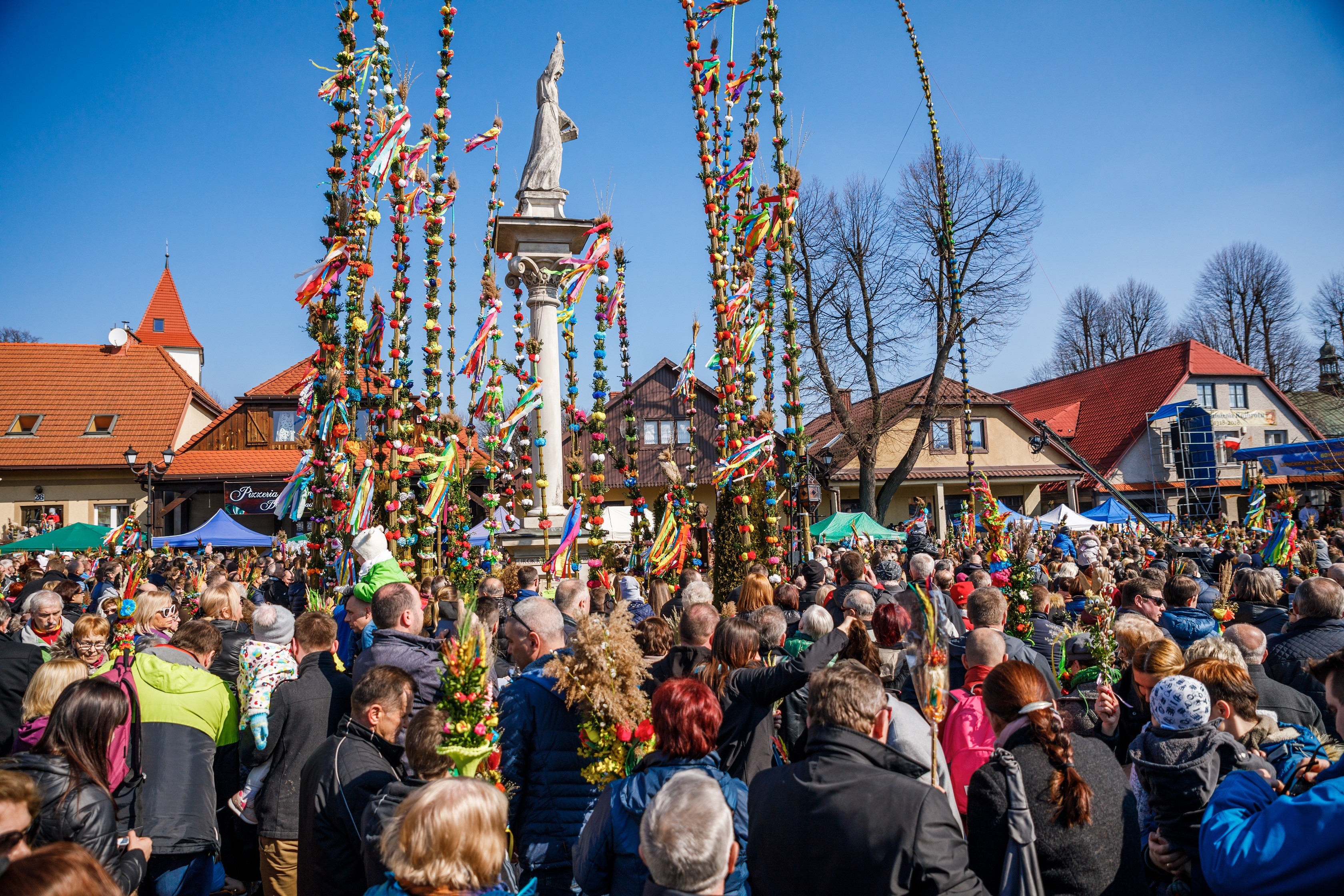 tłum ludzi z wysokimi palmami wokół pomnika